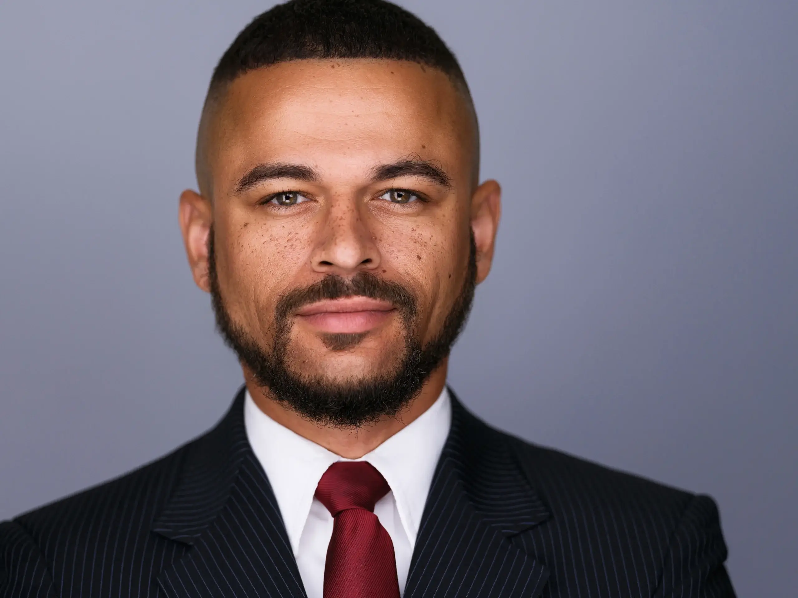 Houston attorney headshot of a bearded man in a dark suit and red tie on a gray backdrop