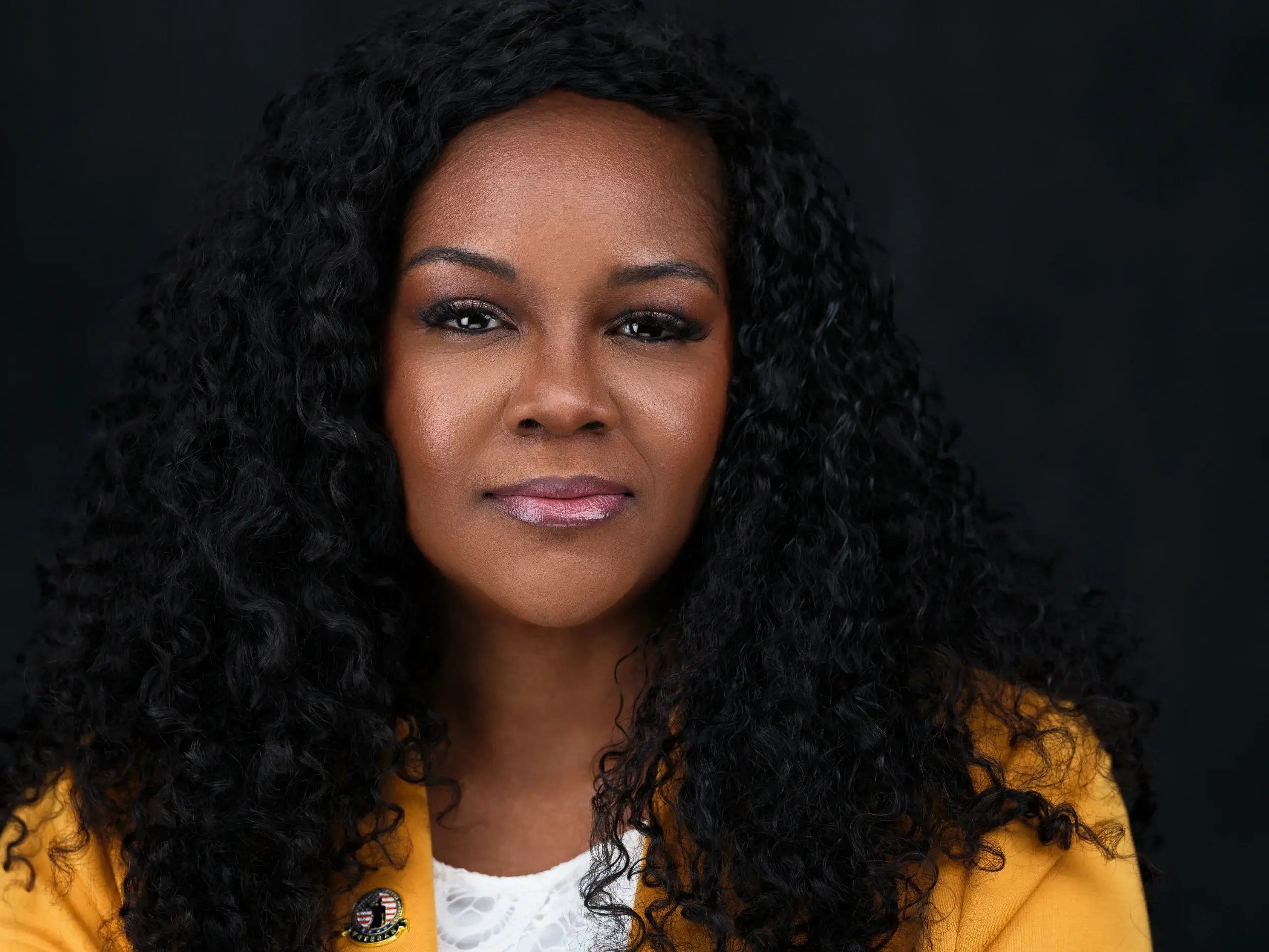Houston attorney headshot of a woman with curly hair in a yellow jacket on a dark backdrop