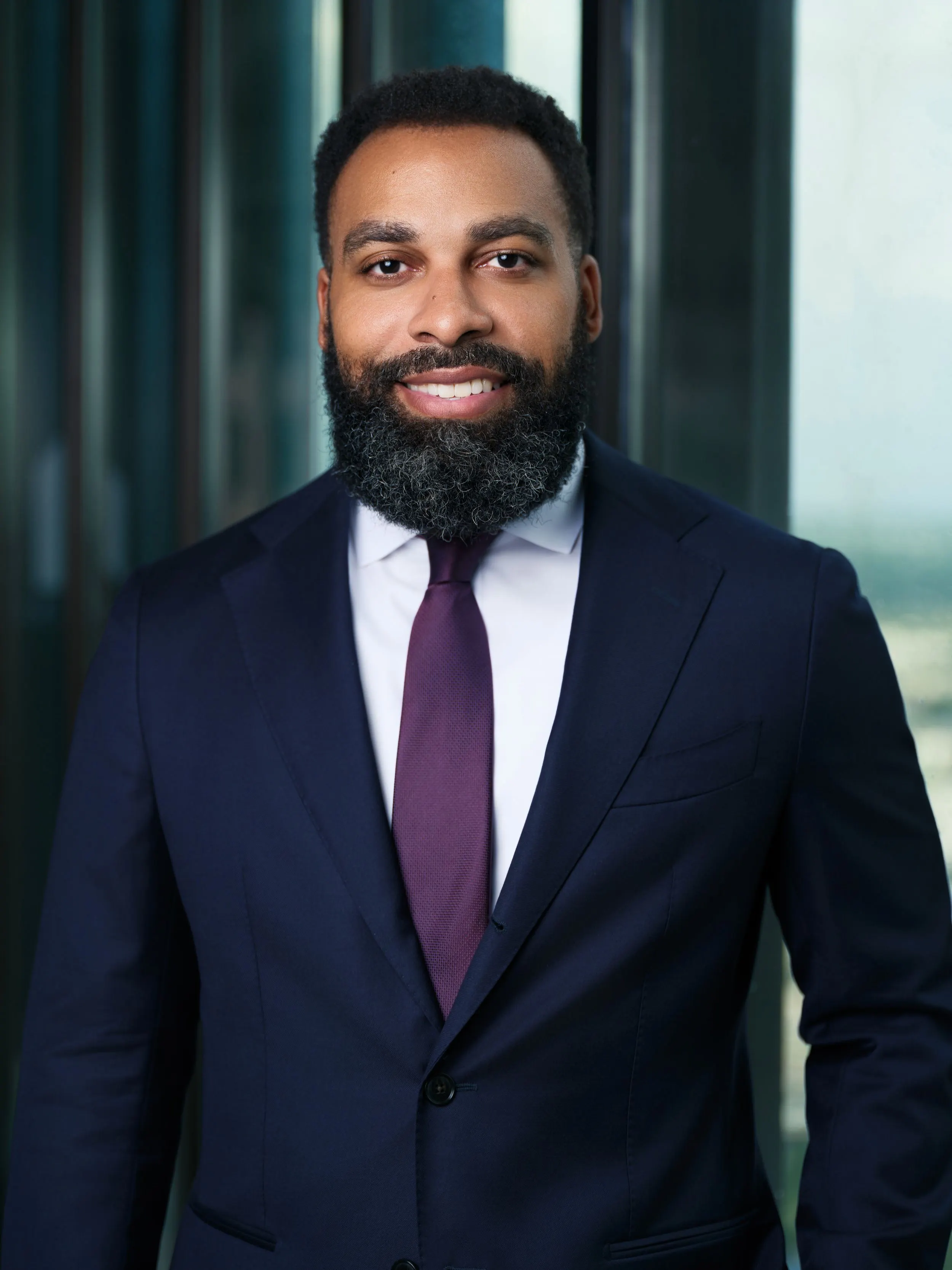 Smiling Egbuonu Law attorney in a navy suit and purple tie by a high-rise window in Downtown Houston