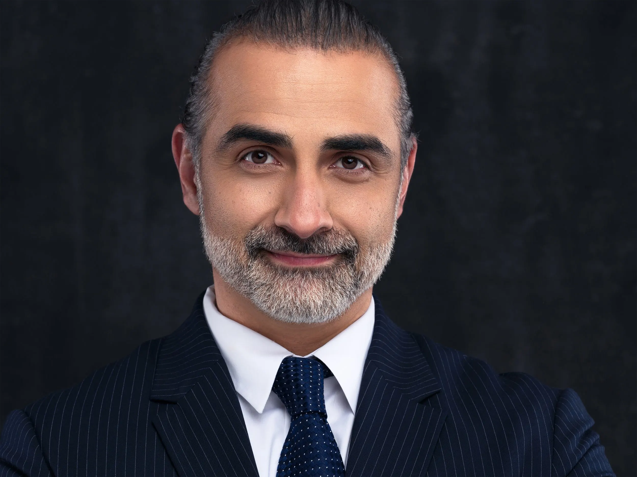 Ghuneim Law Firm attorney with silver hair in a navy pinstripe suit and blue tie on a dark backdrop