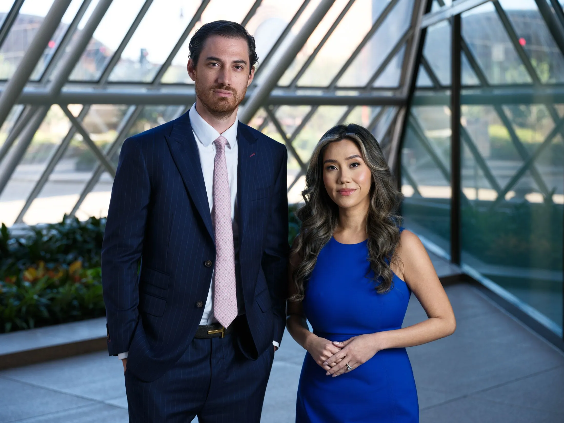 Ryan and Kylie Loya of Loya Law standing together in a sunlit glass atrium in Downtown Houston