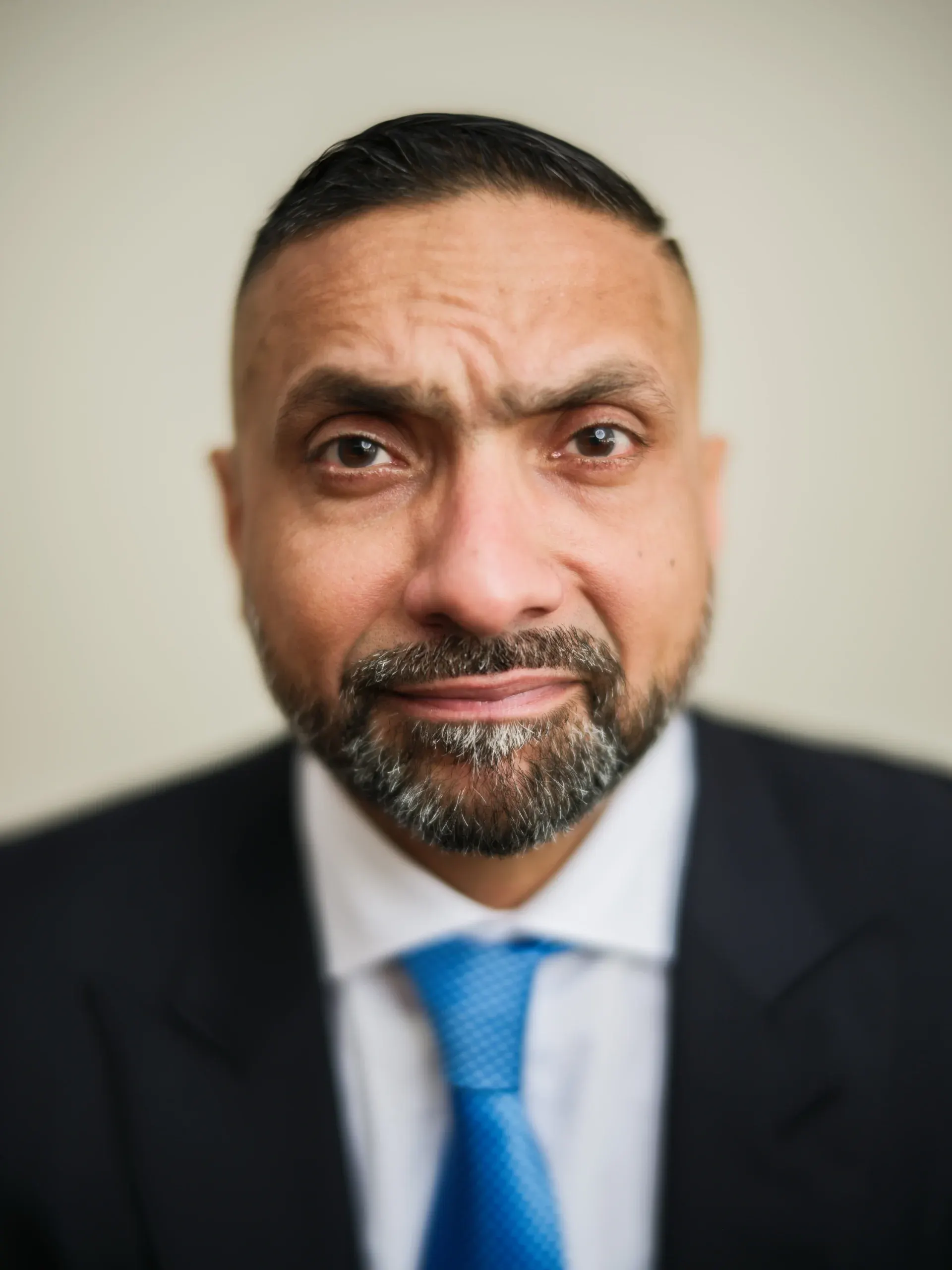 Close-up Houston headshot of a bearded man in a white shirt and blue tie on a light backdrop