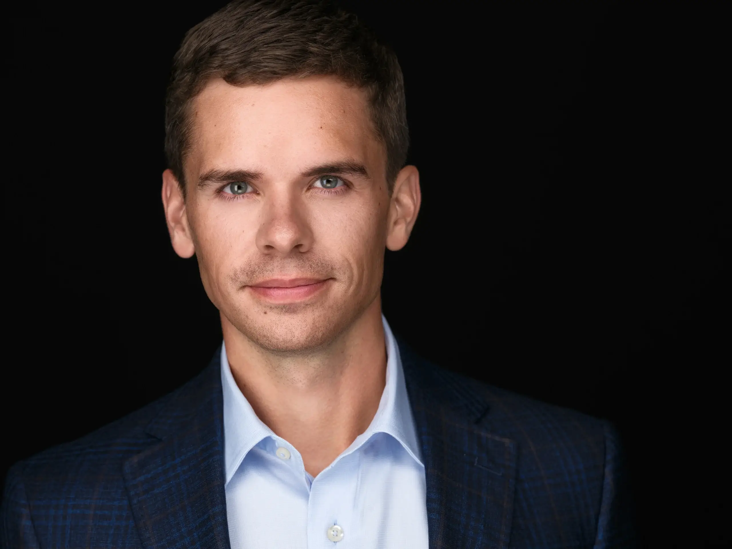 Executive headshot of a man in a navy blazer and open-collar blue shirt on a black studio backdrop in Houston