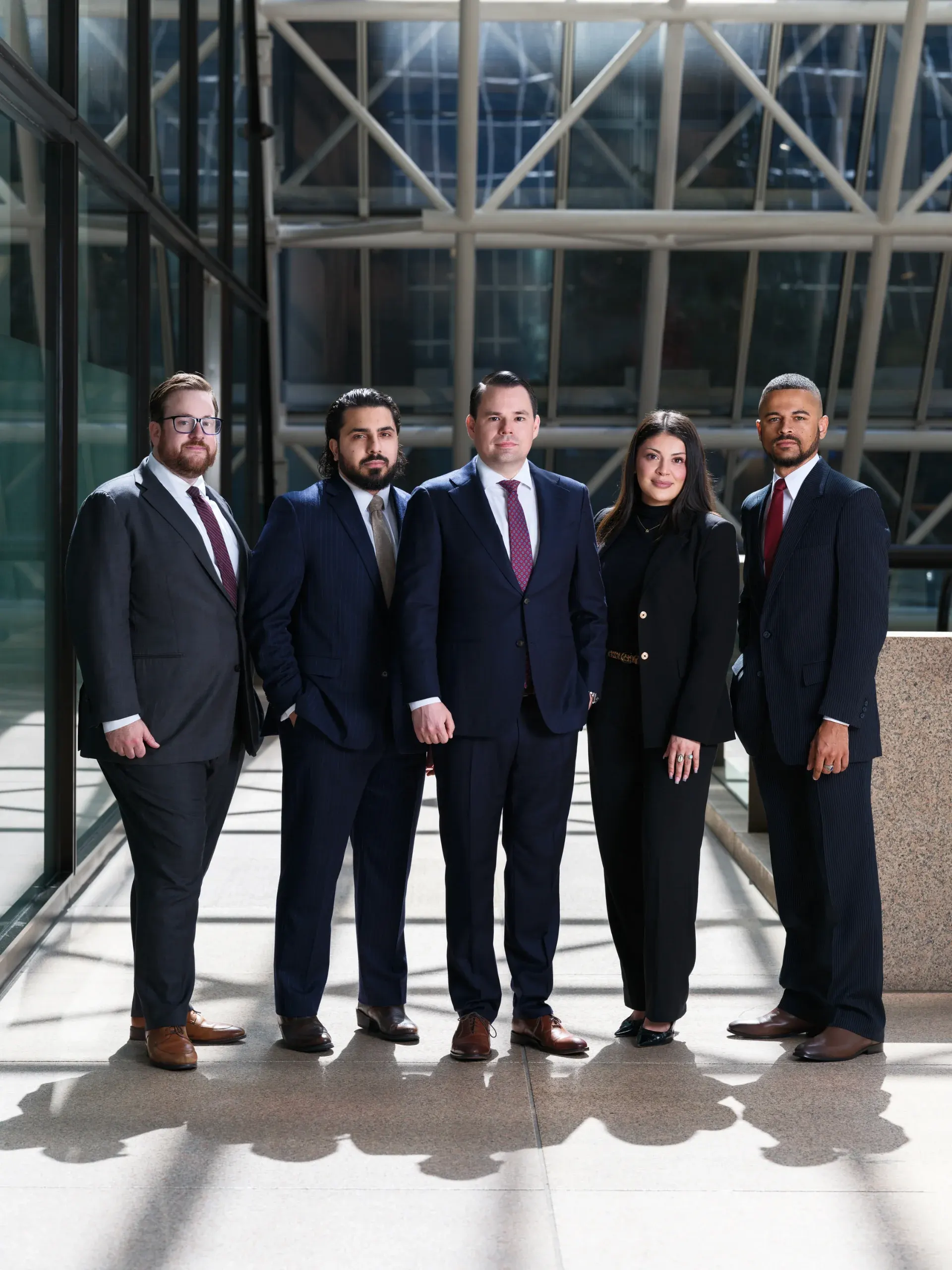 Houston law firm team of five in dark suits standing in a sunlit glass atrium