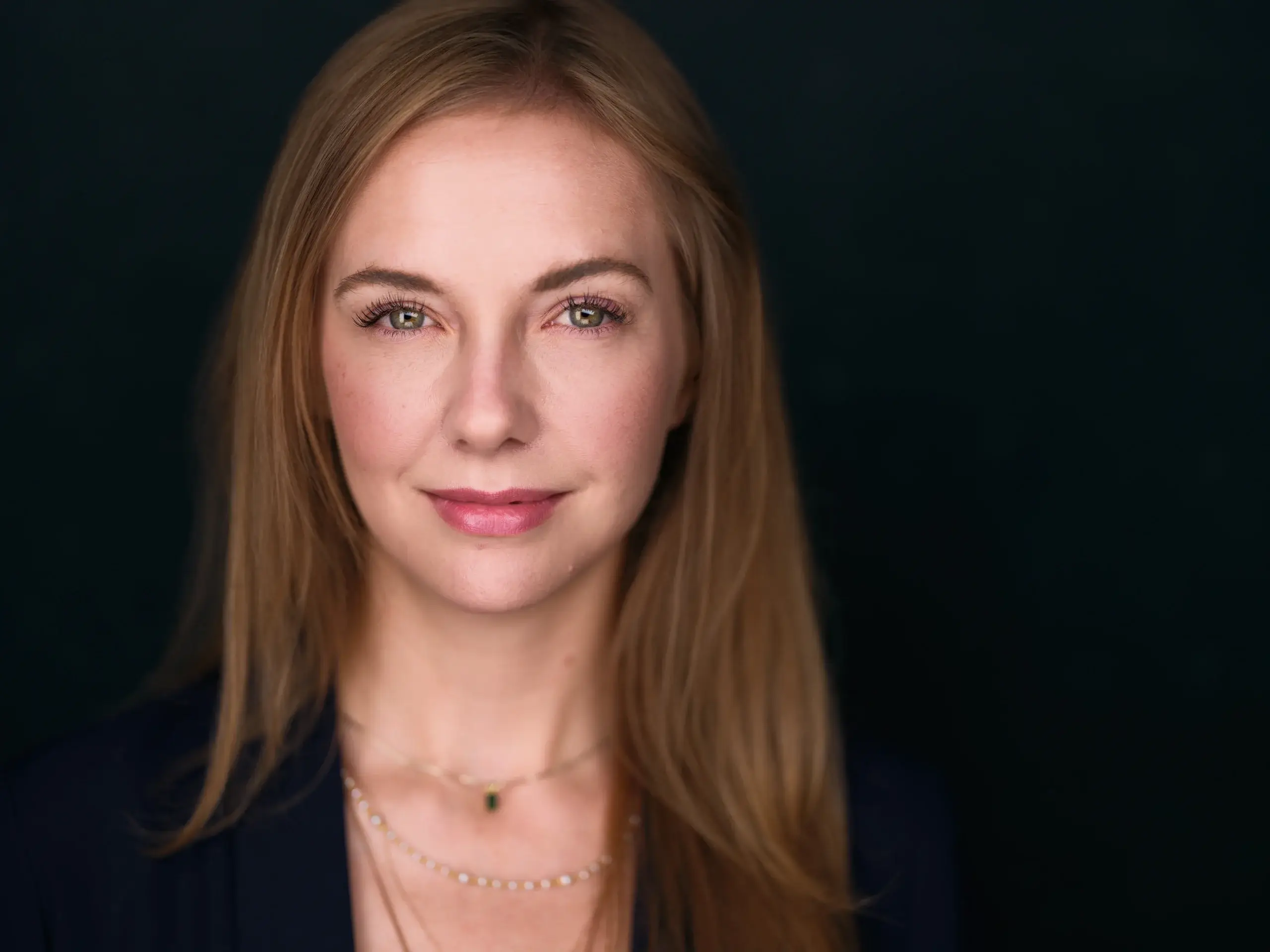 Houston headshot of a woman with long auburn hair and a gold necklace on a dark studio backdrop