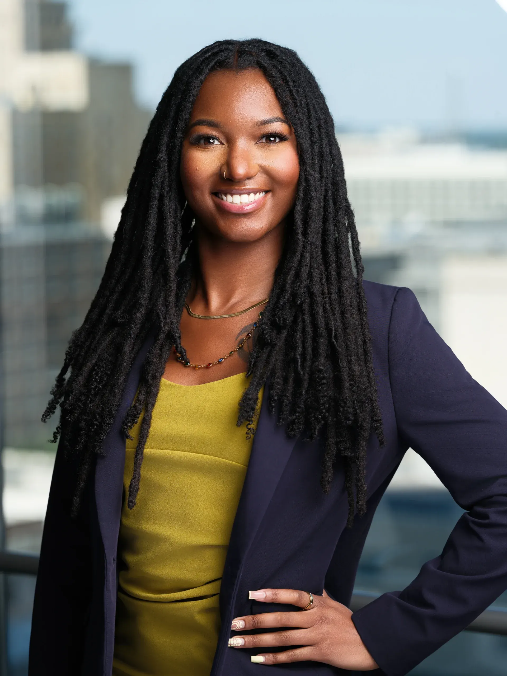 Houston corporate headshot of a smiling woman with long braids in a navy blazer and yellow top by an office window