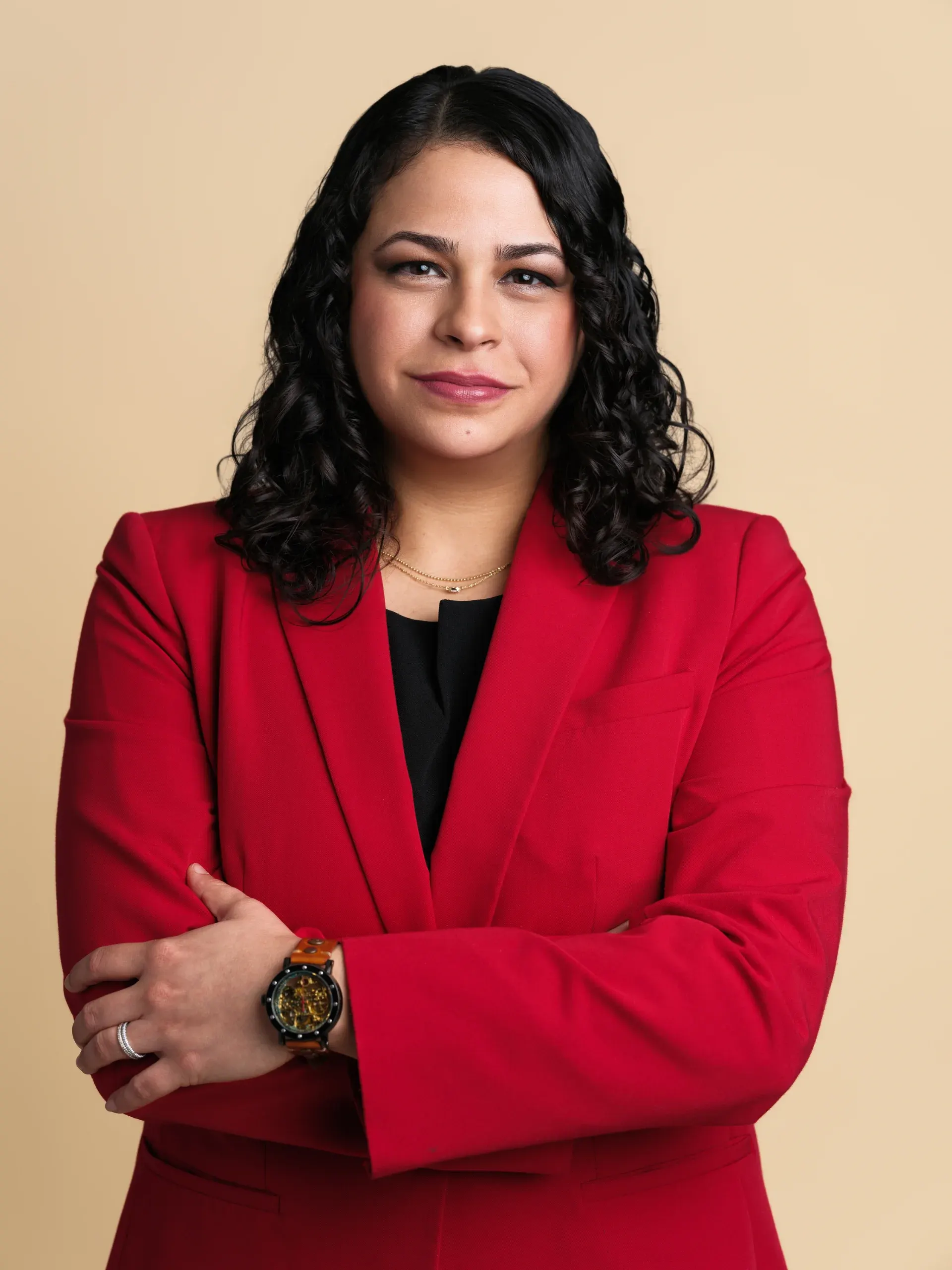 Houston headshot of a woman in a red blazer, arms crossed, on a warm tan backdrop