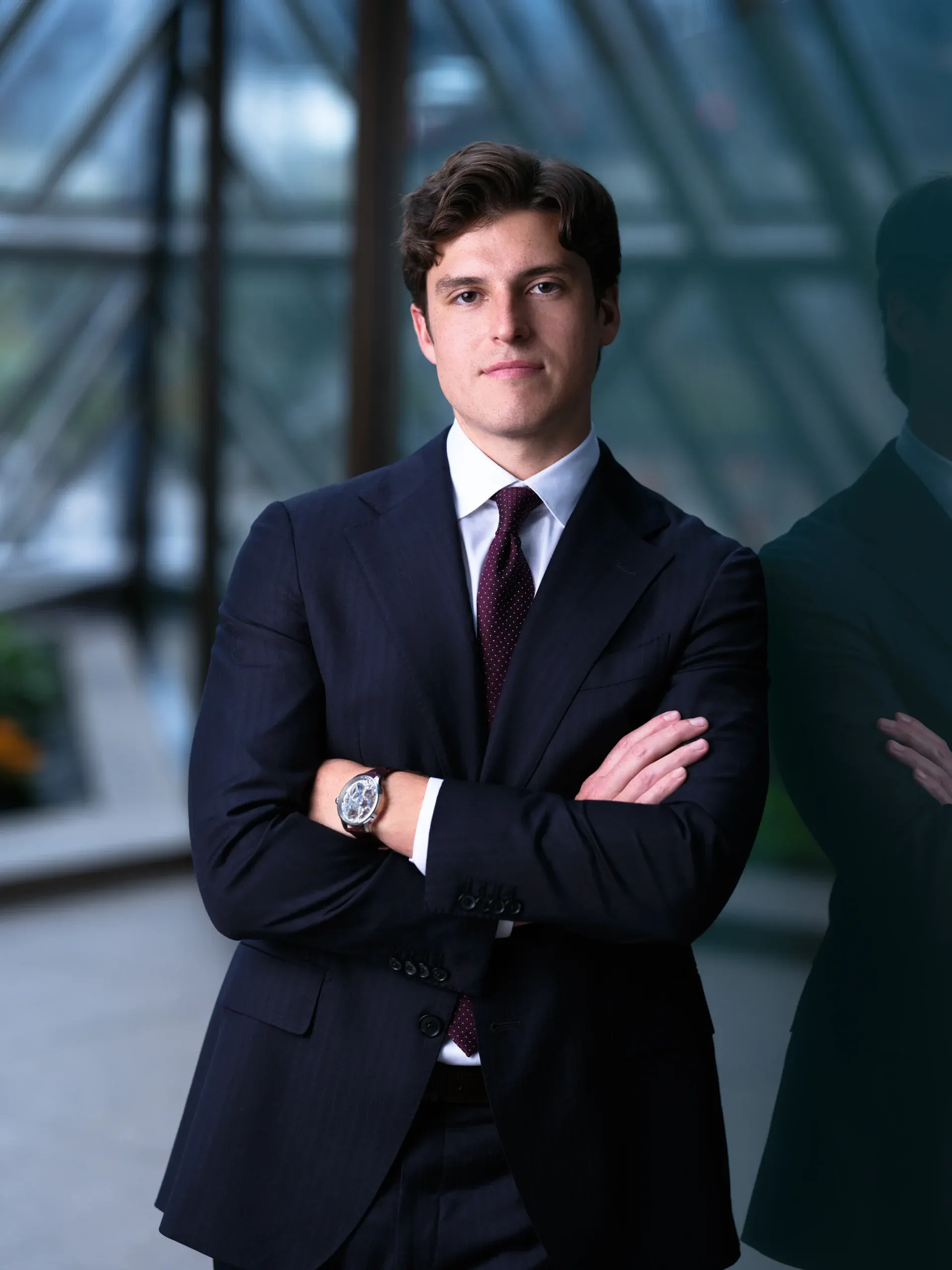 Young Houston attorney in a navy suit and burgundy tie, arms crossed, in a glass office atrium